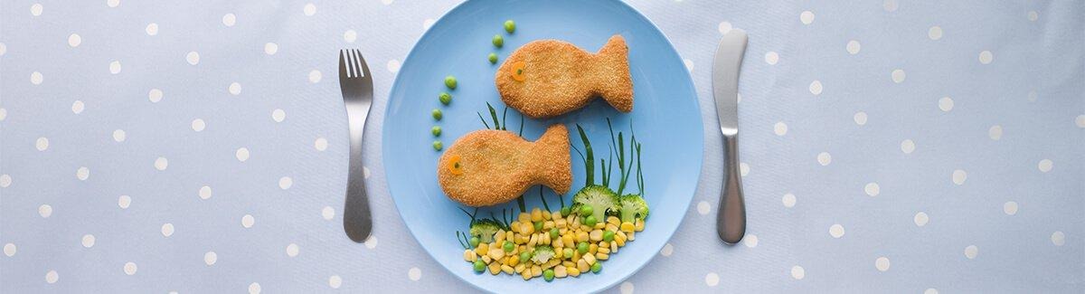 Tostada con queso y verduras formando la figura de un pez, en un plato blanco con fondo azul. El texto en español promueve el desarrollo intelectual de los niños con omega 6 y 3. Se muestra una lata de PediaSure en la esquina inferior derecha.