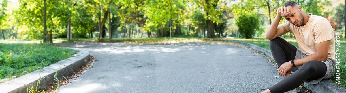 Cuerpo de persona con ropa deportiva, sentada en una acera de un pasto al aire libre