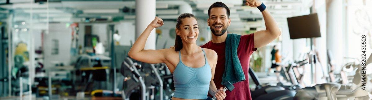 Pareja de adultos en el gimnasio, sonriendo, enseñando sus músculo