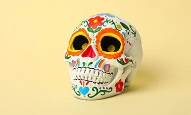 Configuración colorida con elementos típicos de un "Altar de Muertos". Hay una figurita de un esqueleto con un sombrero azul