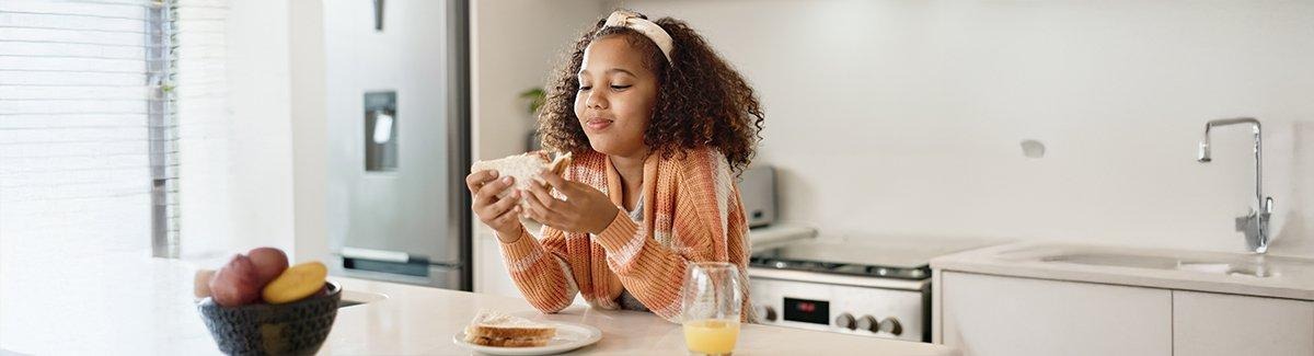 Niña desayunando sandwich con jugo de naranja