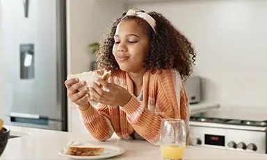 Niña desayunando sandwich con jugo de naranja