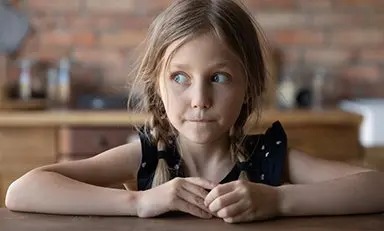 Niña sentada en el comedor mirando a su derecha