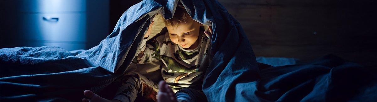 Niño bajo una cobija viendo videos