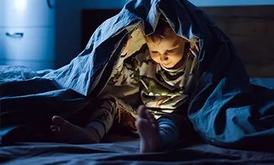 Niño bajo una cobija viendo videos