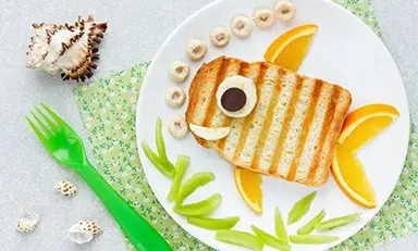 Rebanada de pan tostado en un plato blanco sobre un fondo azul. La tostada está cubierta con queso, rodajas de albaricoque, una rodaja de aceituna negra y una rodaja de aceituna verde.