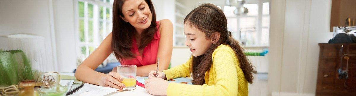 Un adulto y un niño sentados en una mesa. El adulto usa una laptop, mientras que el niño sostiene un cuaderno y lleva audífonos.