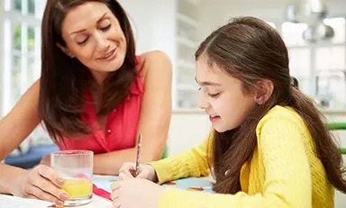 Un adulto y un niño sentados en una mesa. El adulto usa una laptop, mientras que el niño sostiene un cuaderno y lleva audífonos.