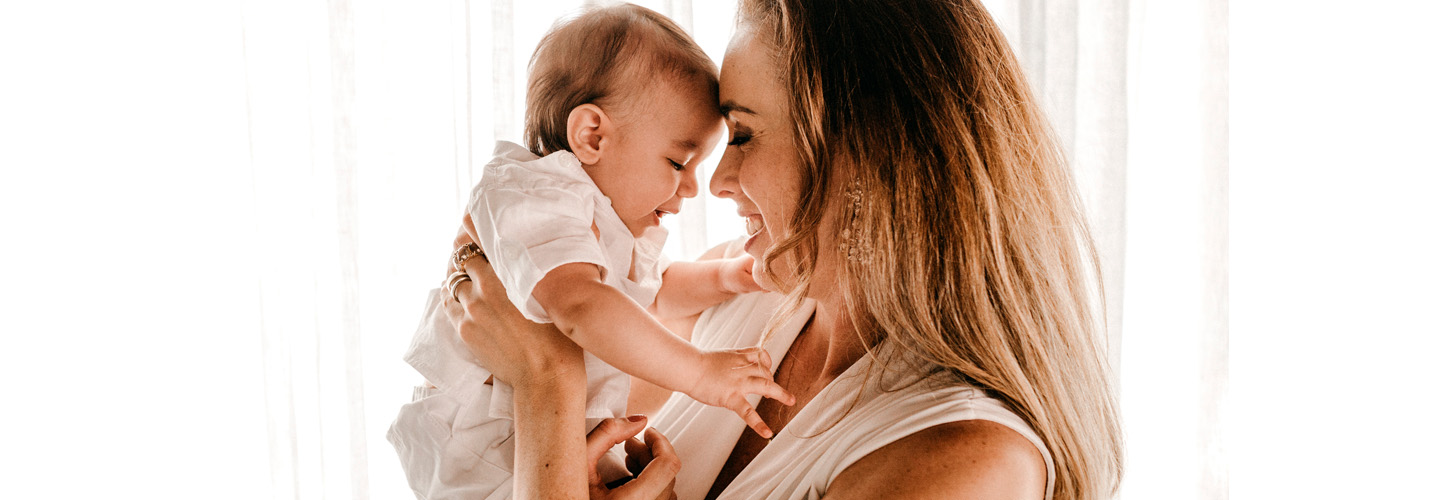Mujer sostiene a su bebé frente a frente, sonriéndole