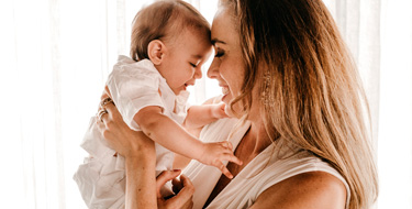 Mujer sostiene a su bebé frente a frente, sonriéndole