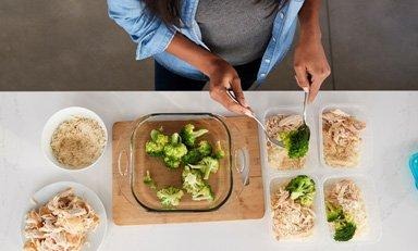 Mujer empacando cuatro almuerzos para llevar con brócoli, arroz y pollo
