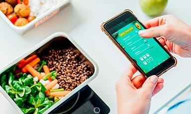 Mujer utilizando una aplicación de registro de comidas con un almuerzo frente a ella en una mes