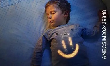 Niño dormido plácidamente en su cama con una carita sonriente dibujada en su pecho