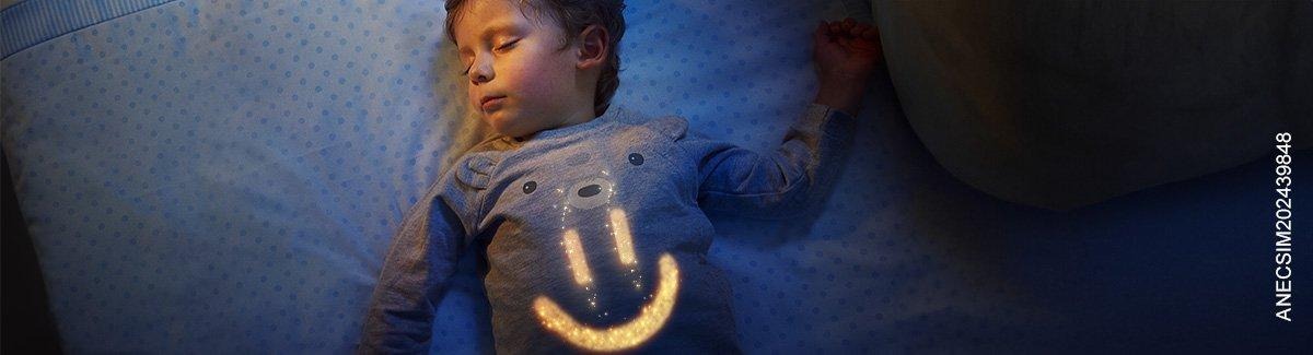 Niño dormido plácidamente en su cama con una carita sonriente dibujada en su pecho