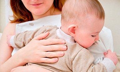 Mama sostiene a su bebe en sus brazos, una de sus manos está  en la espalda del bebe