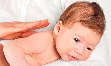 Mamá sostiene a su bebe boca abajo y tiene una mano en la espalda del bebe