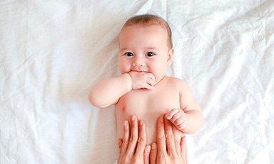 Bebe acostado boca arriba, unas  manos tocan su estómago.