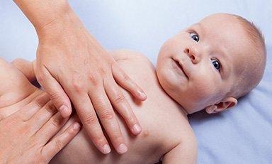 Bebe acostado boca arriba, unas  manos tocan su estómago.