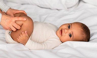 Bebe acostado boca arriba, unas  manos tocan sus piernas