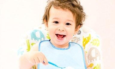 Bebe sonriente toma una cuchara con alimento con su mano derecha.