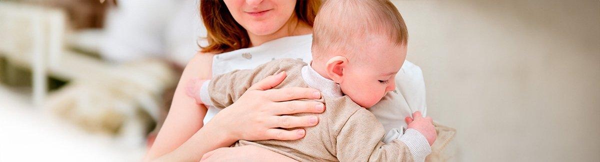Mama sostiene a su bebe en sus brazos, una de sus manos está  en la espalda del bebe