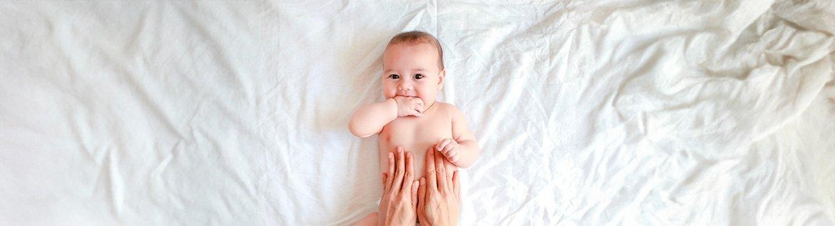 Bebe acostado boca arriba, unas  manos tocan su estómago.