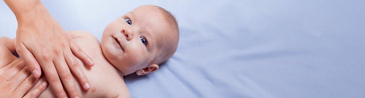 Bebe acostado boca arriba, unas  manos tocan su estómago.