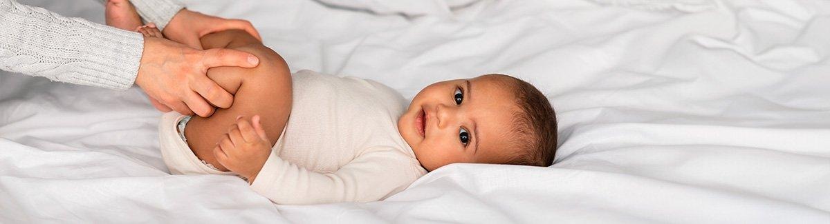 Bebe acostado boca arriba, unas  manos tocan sus piernas