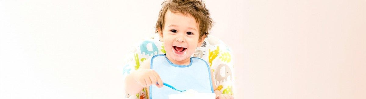 Bebe sonriente toma una cuchara con alimento con su mano derecha.