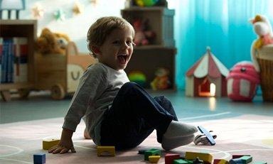 Niño risueño sentado en un cuarto de juegos, rodeado de piezas de madera dispersas por el suelo