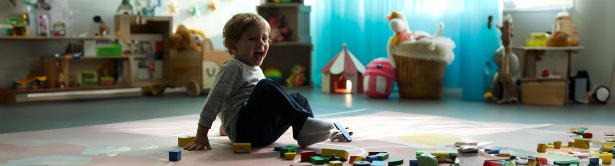 Niño risueño sentado en un cuarto de juegos, rodeado de piezas de madera dispersas por el suelo